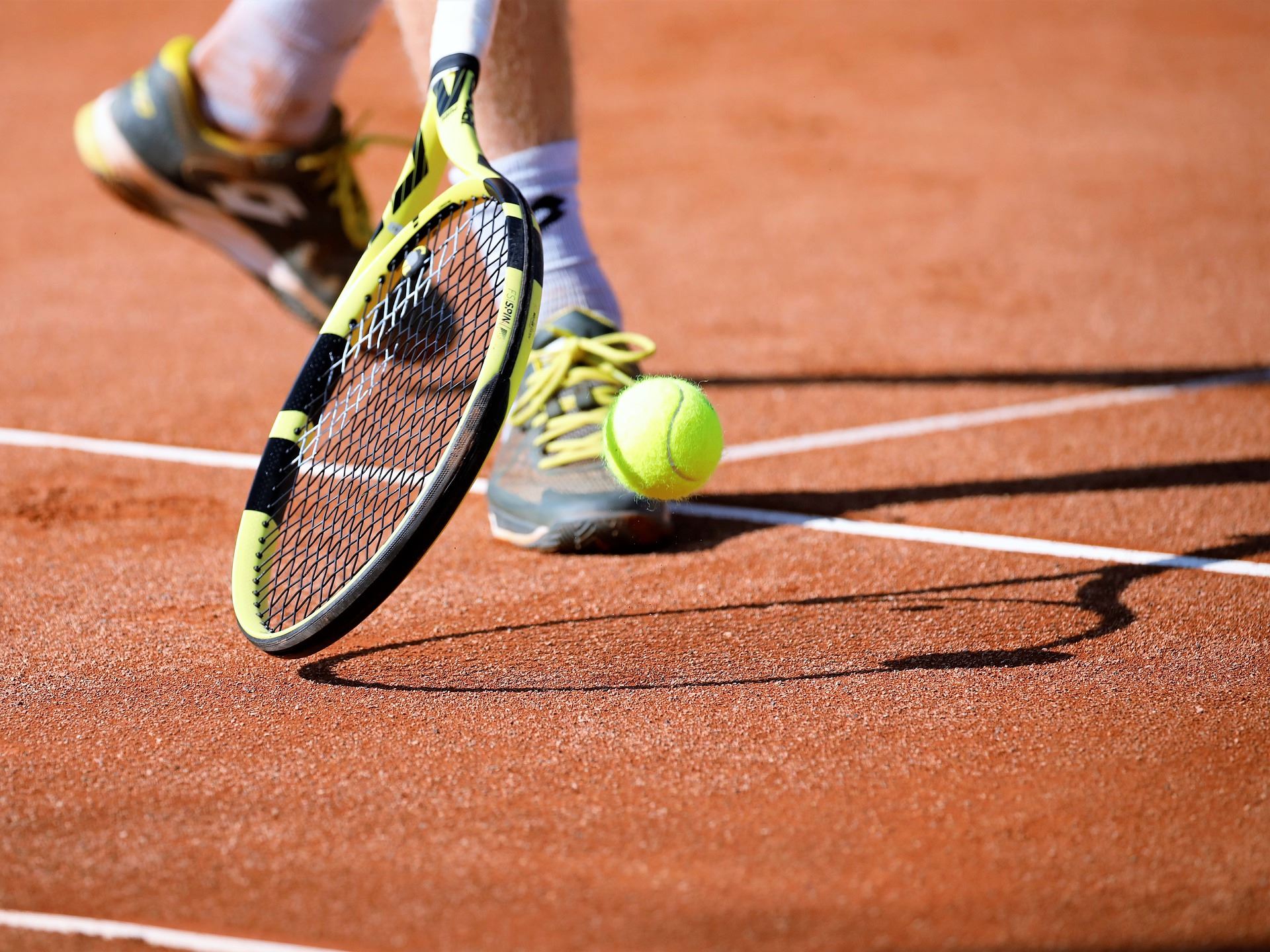 A person reaching for a tennis ball on a tennis court. 